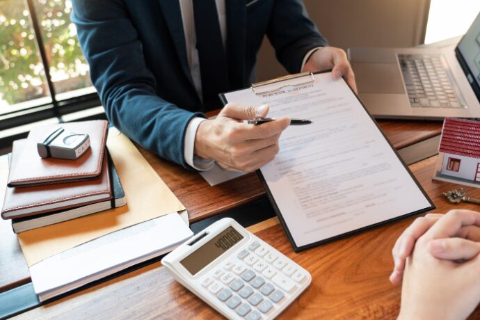 Estate agent explaining rental property investment agreement with documents, calculator, and house model on desk