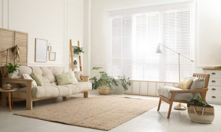 A bright and modern living room with natural wood furniture, indoor plants and large window blinds, representing a calm and well-maintained home.