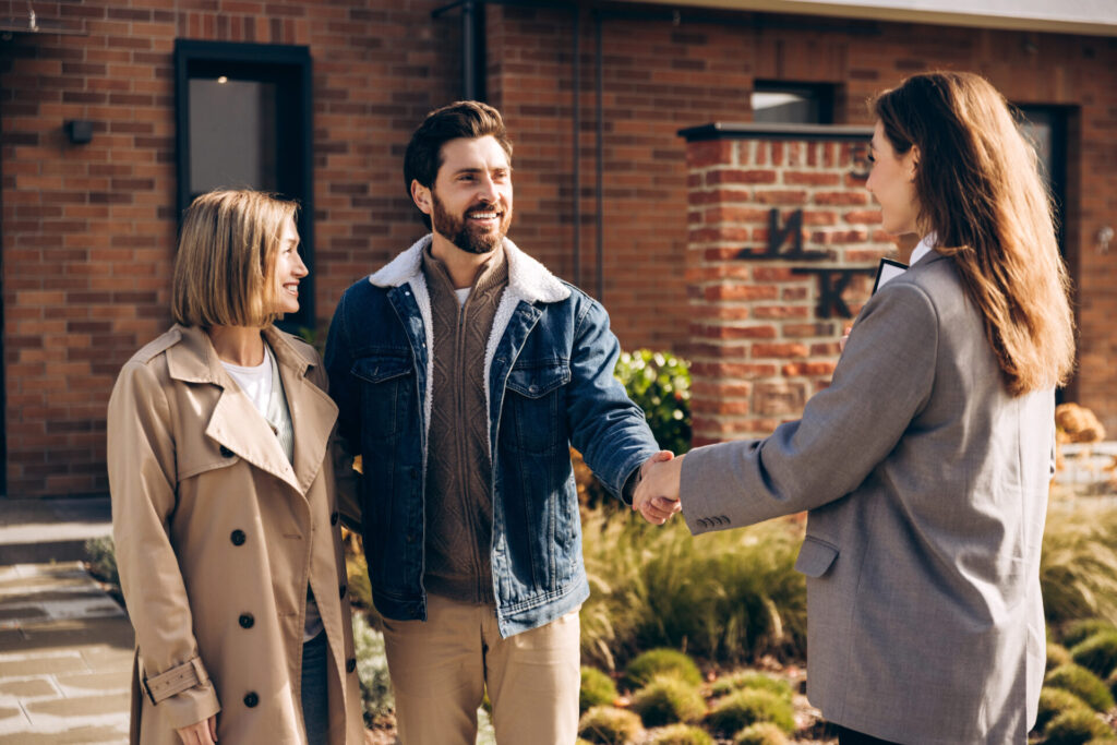 Estate agent shaking hands with homeowners outside a modern property in the South East discussing a house move and property valuation.
